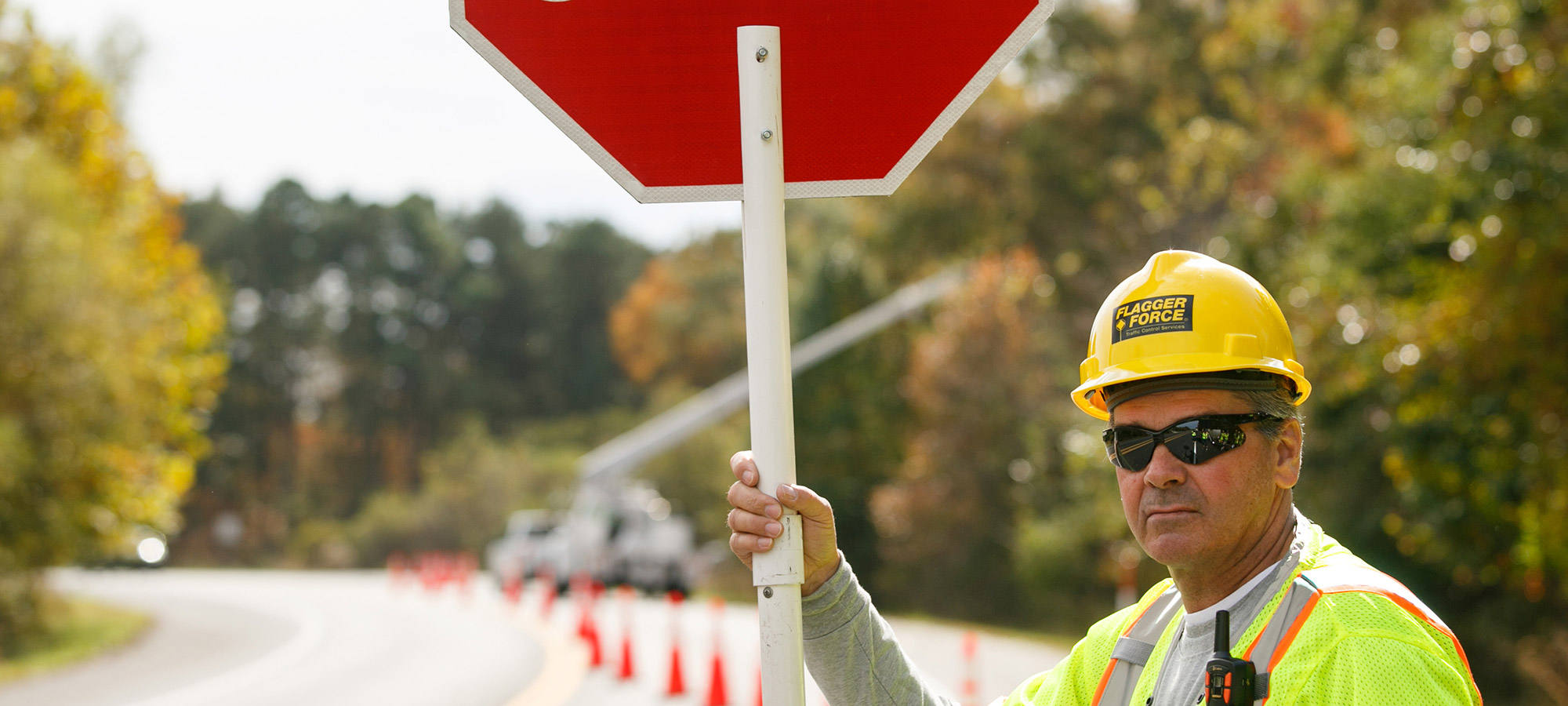 A Flagger Force employee working outdoors, wearing a hard hat, a reflective vest, and holding a sign.